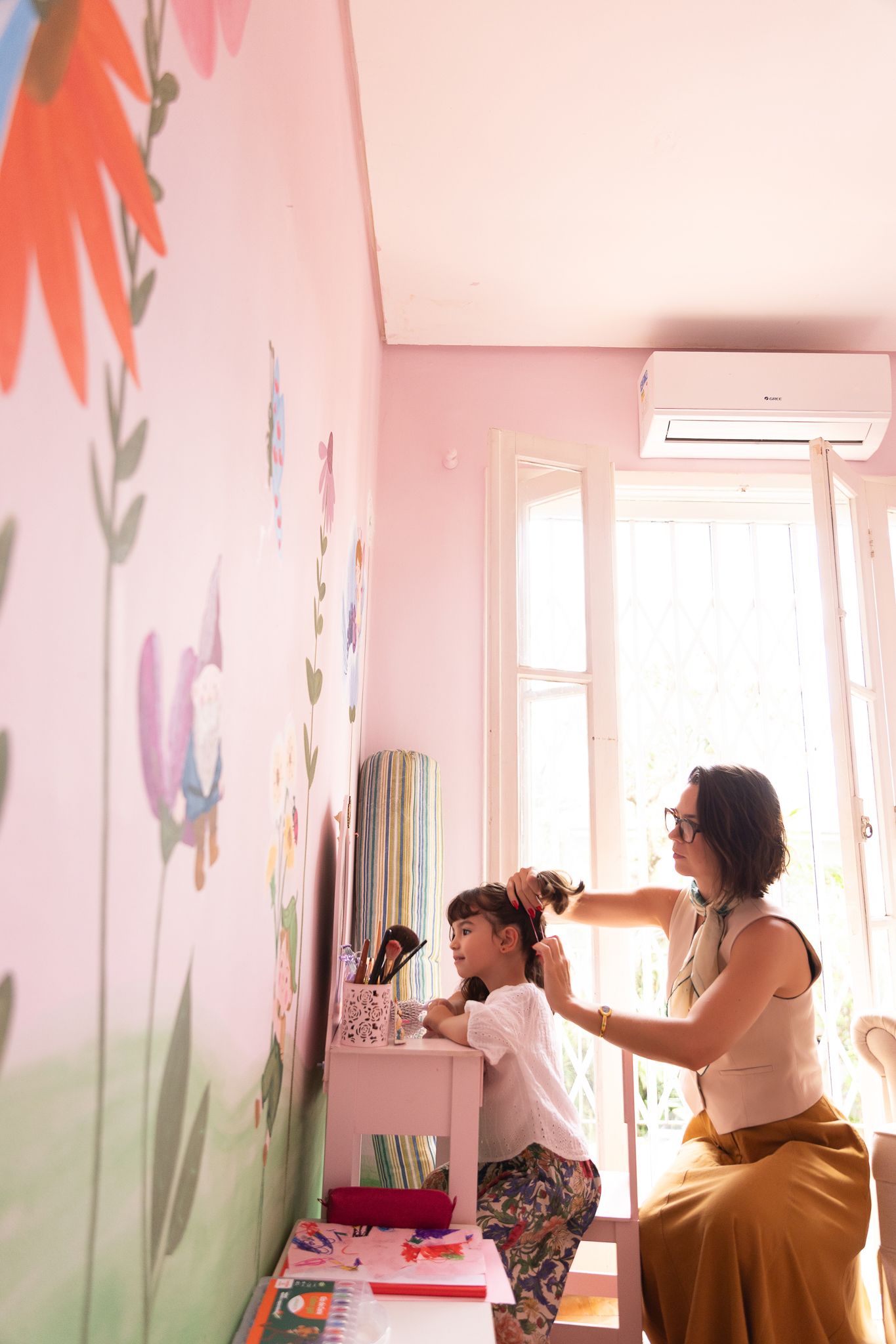Mãe penteia o cabelo da filha num quarto cor-de-rosa
